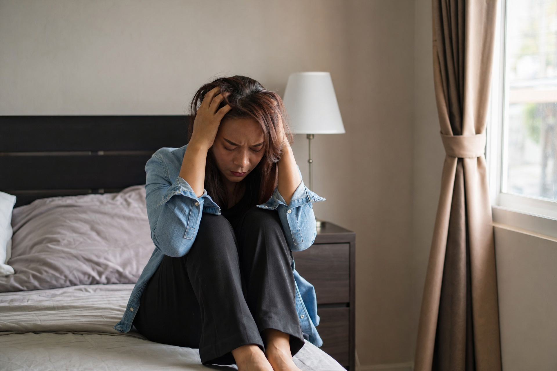 A woman sitting alone with both hands holding her head, feeling overwhelmed.
